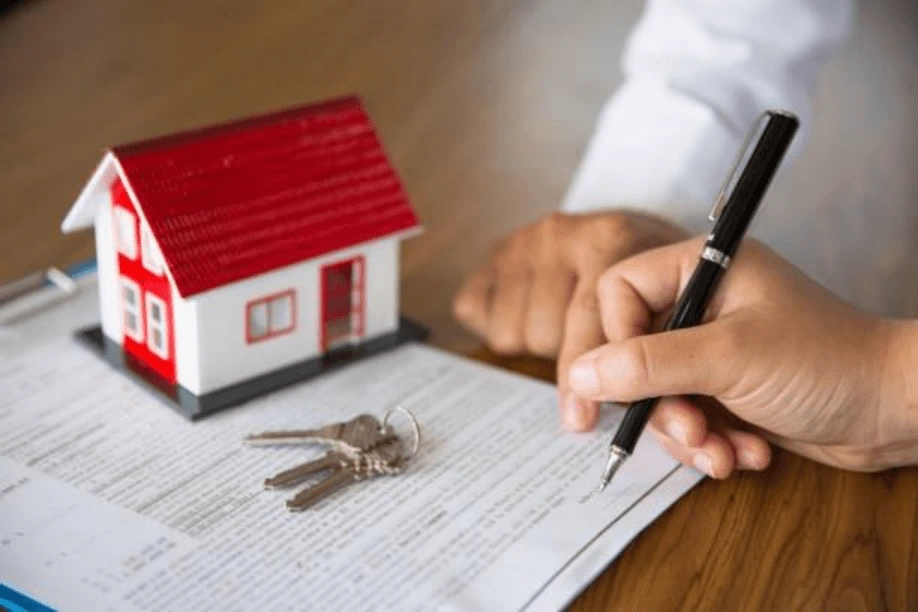 Hand signing UK mortgage agreement with model house and keys